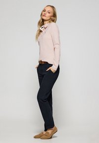 Ljusrosa långärmad polo skjorta med krage, svarta byxor och tan loafers. Har en liten logotyp på skjortan och ett brunt bälte.