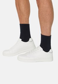 Hvide sneakers med glat læderfinish og gummisåler, kombineret med marineblå crew-strømper, der er synlige over ankelhøjde.