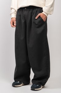 Pantaloni neri a gamba larga con cintura elasticizzata e bottone anteriore. Presentano tasche laterali e una texture liscia, abbinati a sneaker.