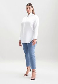White long-sleeve button-up shirt with a pointed collar, paired with light blue denim jeans and black heeled sandals. Smooth, tailored fit.