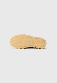 Beige rubber sneaker sole with textured grip and raised wavy pattern, placed on a plain white background.