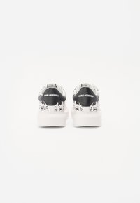 Bílé tenisky s černým patkem, s opakovaným vzorem koček, hladkým povrchem a gumovou podrážkou. Logo značky na patě.