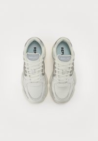 Zapatillas deportivas blancas con superposiciones de malla y cuero, que presentan una franja de acento gris, cordones redondos y un cuello acolchado. El interior muestra un forro azul claro.