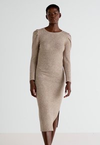 Abito in maglia di un tono beige chiaro, con texture rigata, maniche lunghe, scollo a giro e uno spacco laterale per facilitare i movimenti.