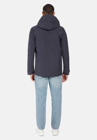 Laivansinis huppari, jonka pinnassa on sileä viimeistely, ja jossa on logo selkäpuolella, yhdistettynä vaaleansinisille farkuille ja valkoisille lenkkareille.