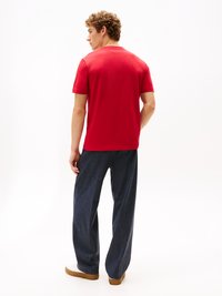 Tricou roșu din bumbac cu guler rotund, asortat cu pantaloni largi de culoare albastru închis. Adidașii albi completează ținuta.