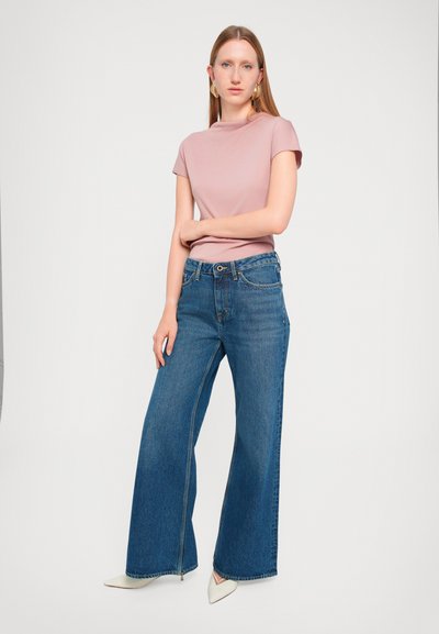 Haut rose clair à manches courtes associé à un jean en denim bleu à jambes larges et des talons blancs pointus. Présente un design simple et des lignes épurées.