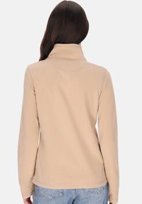 Beige színű fleece pulóver magas gallérral, hosszú ujjal és sima textúrával. Jellemzője az egyszerű, letisztult dizájn, látható logók vagy minták nélkül.