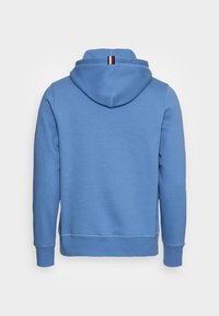 Sudadera con capucha azul de tela suave, con capucha ajustable con cordón, puños acanalados y un pequeño detalle de franjas tricolores en el cuello.