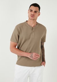 Szaffrán színű, rövid ujjú henley póló, textúrált anyagból készült, kerek nyakkal, háromgombos patenttel és kontrasztos varrási részletekkel.
