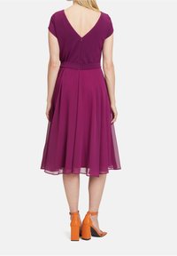 Fialové midi šaty s krátkými rukávy a V výstřihem, s dobře padnoucím pasem a volnou sukní. Nalezeno s oranžovými sandály na blokovém podpatku.