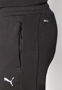 Sorte sportsbukser med ribbet talje og sidelomme med lynlås. Har "DRYCELL"-mærke og hvidt Puma-logo på benet. Blødt stof.