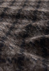 Tissu de laine texturé en marron et noir, présentant un motif moucheté. La surface est douce avec un léger éclat et une profondeur due aux plis.