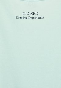 Tissu côtelé bleu clair avec un col rond. Texte "CLOSED Creative Department" imprimé en bleu foncé au dos.