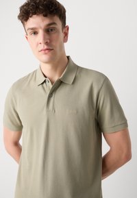 Maslinasto zelena polo majica od teksturiranog pamuka, s tri gumba i diskretnim izvezenim logotipom na prsima.