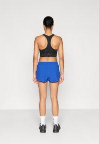 Top deportivo negro con diseño de espalda racer, combinado con pantalones cortos azules con cintura elástica. Zapatillas negras y calcetines blancos completan el conjunto.