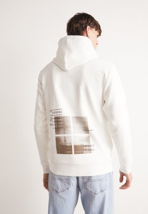Sweatshirt à capuche blanche avec un design graphique texturé marron au dos, comportant quatre sections carrées et des accents linéaires. Matériel doux.