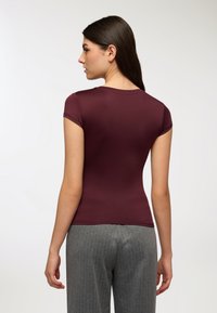 T-shirt aderente color borgogna con maniche corte e collo rotondo. Tessuto liscio, abbinato a pantaloni grigi a righe sottili, caratterizzati da una vestibilità casual.