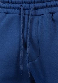 Marineblaue Sweatpants aus weichem Material, mit elastischem Bund, Zugband und Seitentaschen. Glatte Textur mit einem einfarbigen Muster.