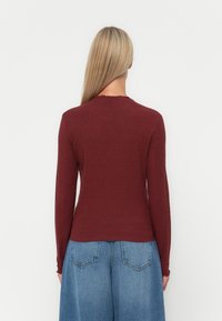 Burgundy pitkähihaisen ribbivetimen kanssa, jossa on aaltoileva kaula-aukko, yhdistettynä leveisiin sinisiin denimhousuihin, joissa on takataskut ja haalistunut pinta.