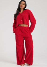Rød fleece loungewear-sæt bestående af en cropped, knap-op top med hætte og løstsiddende, elastisk-liv bukser for komfort.
