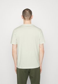 Svetle zelené bavlněné tričko s krátkým rukávem, kulatým výstřihem a rovnými lemy, zobrazené zezadu. Jednoduchý design s jemnou texturou.