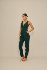 Ολόσωμη φόρμα σε σμαραγδί πράσινο με βαθύ V ντεκολτέ, εφαρμοστή σιλουέτα, φαρδιές τιράντες και πλαϊνές τσέπες. Συνδυασμένη με χρυσές λεπτομέρειες και ψηλοτάκουνα.