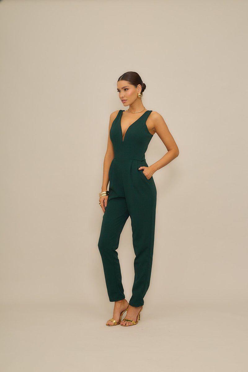 Ολόσωμη φόρμα σε σμαραγδί πράσινο με βαθύ V ντεκολτέ, εφαρμοστή σιλουέτα, φαρδιές τιράντες και πλαϊνές τσέπες. Συνδυασμένη με χρυσές λεπτομέρειες και ψηλοτάκουνα.
