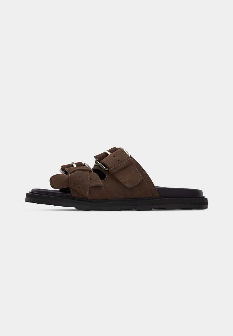 Καφέ δερμάτινο σανδάλι με δύο ρυθμιζόμενους ιμάντες με αγκράφες και μαύρη ελαστική σόλα, απεικονιζόμενο σε πλάγια όψη.