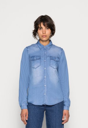 Lys blå denimskjorte med lange ermer, knappestolpe, to brystlommer og spiss krage; glatt tekstur, litt falmet finish.