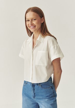 White short-sleeve button-up shirt with a pocket, made of cotton. Paired with blue denim jeans. Simple design and relaxed fit.