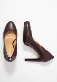 Leather high-heeled shoes in burgundy, with a rounded toe and a textured dark wood heel. Features a logo detail on the back.