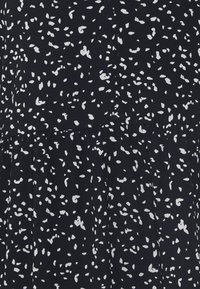 Tissu noir avec de petites taches blanches irrégulières dans un motif dispersé, avec une couture et de légers fronces près du milieu.
