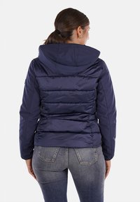 Giacca a vento blu navy con cappuccio, caratterizzata da un design trapuntato, polsini elastici e una forma aderente, mostrata dal retro.