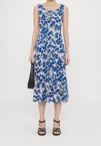 Robe fleurie bleue avec un corsage ajusté et une jupe évasée, confectionnée dans un tissu léger, présentant des motifs de feuilles blanches et une texture lisse.