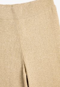 Leggings de punto acanalado en color beige con una cinturilla ancha y una superficie texturizada. El material parece suave y ligeramente elástico. Sin patrones o acentos distintivos.