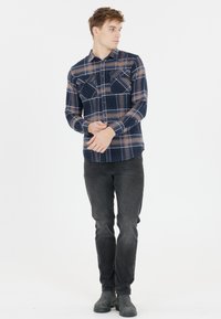 Marine ruit overhemd met lange mouwen en lichtbruine accenten, twee borstzakken en knoopmanchetten, gecombineerd met donkere slim-fit jeans en grijze laarzen.