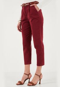 Pantaloni cropped bordeaux con vita alta e pieghe, abbinati a tacchi a strappo marroni. I pantaloni presentano passanti per cintuira e una texture di tessuto liscia.