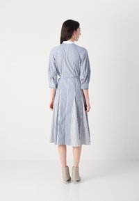 Pruhované šaty v modrej a bielej farbe s tromi štvrtinovými rukávmi, opaskom v pase a rozšírenou sukňou. Outfit dopĺňajú béžové členkové čižmy.