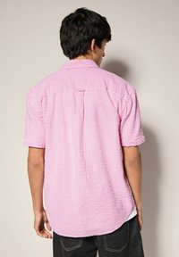 Kurzarmhemd im rosa-weißen Karomuster, mit Rückenpasse, lockerem Schnitt und geradem Saum mit seitlichen Schlitzern.