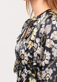 Černá květinová blůza s volánkovými detaily. Obsahuje velké žluté a purpurové květy, složité vzory a hladký saténový povrch.