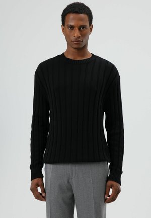 Zwarte geribbelde gebreide trui met een klassieke ronde hals, lange mouwen en een gestructureerde afwerking, gecombineerd met lichtgrijze broek.