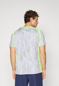 Szürke sportpóló nedvességelvezető anyagból, neonzöld díszítéssel a vállakon és az oldalakon, valamint kör alakú nyakkivágással.