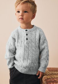 Pull-over en laine bleu clair douce tricotée en torsades, avec trois boutons noirs au col, poignets et ourlet côtelés. Design élégant.