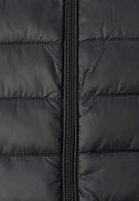 Svart boblejakke med vertikal glidelås, quiltet design og glatt tekstur. Stoffet har en blank overflate med vannavvisende finish.