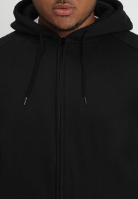 Black zip-up hoodie made from soft, textured fabric; features a drawstring hood and a full-length zipper. Simple, minimalist design.
