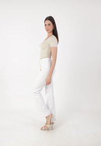 Top de manga corta beige combinado con pantalones blancos de cintura alta con detalles de botones. Sandalias de tacón con tiras beige completan el conjunto.
