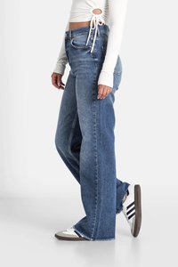 Jeans de campana de cintura alta en denim azul medio con dobladillo deshilachado, combinados con una camiseta blanca de manga larga y zapatillas clásicas en blanco y gris.