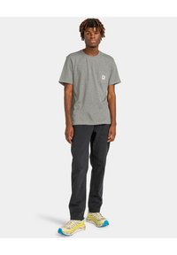 Grå kortærmet t-shirt med en brystlomme, kombineret med sorte bukser og gule sneakers med blå detaljer. Simpelt, afslappet design.