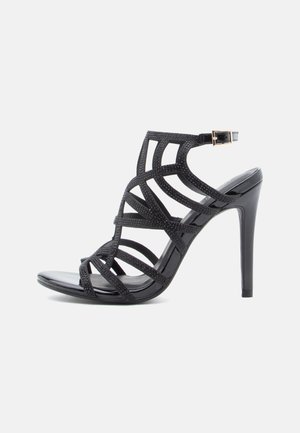 Sandale noire à talons hauts avec un design à lanières, en matériau texturé, à bout ouvert et équipée d'une sangle réglable à la cheville avec une boucle.